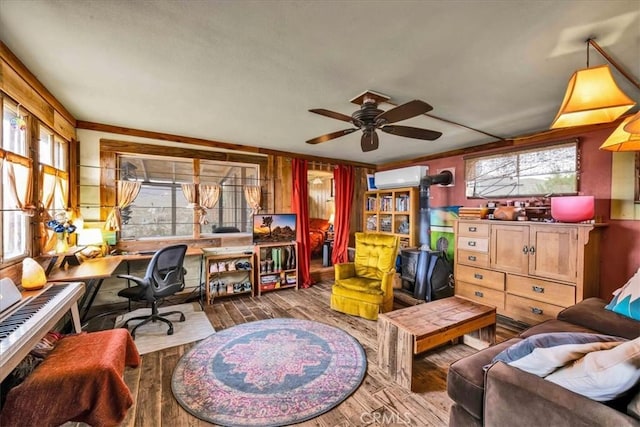 home office featuring a wall mounted air conditioner, a ceiling fan, wood finished floors, crown molding, and a wood stove