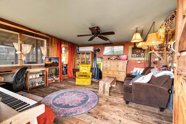 interior space featuring a wall mounted AC, a wood stove, ceiling fan, and wood-type flooring