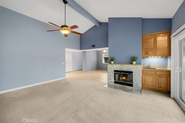 unfurnished living room featuring high vaulted ceiling, a sink, ceiling fan, beamed ceiling, and light colored carpet