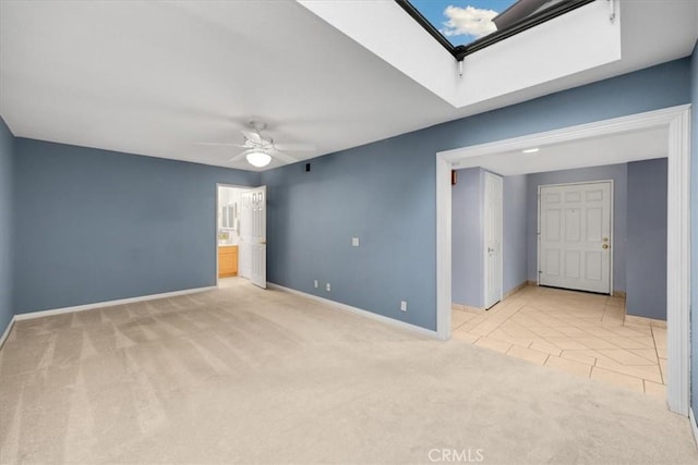 carpeted empty room with tile patterned floors, baseboards, a skylight, and a ceiling fan