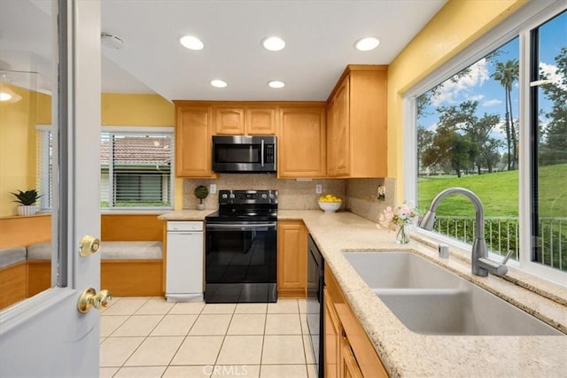 kitchen featuring light tile patterned floors, light stone countertops, a sink, decorative backsplash, and black appliances