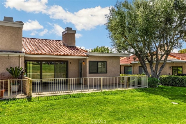 back of house with a tile roof, a lawn, a chimney, and stucco siding