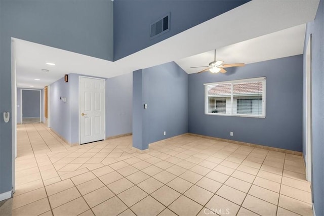 unfurnished room with a towering ceiling, visible vents, light tile patterned flooring, and a ceiling fan