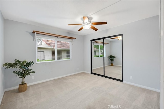 empty room with ceiling fan, light carpet, and baseboards