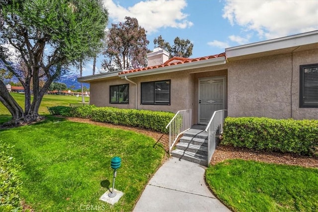 view of exterior entry featuring a tile roof, a lawn, and stucco siding