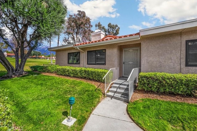 property entrance with a yard, a tiled roof, a chimney, and stucco siding