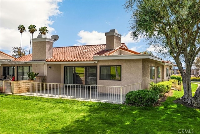 back of property with a chimney, a yard, a tile roof, and stucco siding
