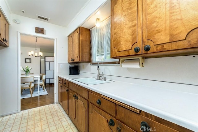 kitchen with brown cabinetry, visible vents, an inviting chandelier, a sink, and light countertops