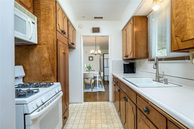 kitchen with visible vents, brown cabinets, a sink, white appliances, and light floors