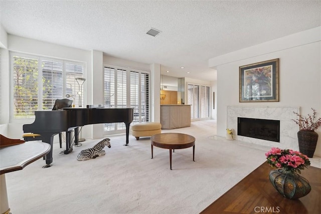 carpeted living area featuring a wealth of natural light, visible vents, a textured ceiling, and a high end fireplace