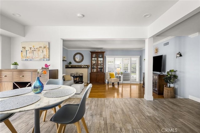 dining space featuring wood finished floors, baseboards, visible vents, a fireplace, and ornamental molding