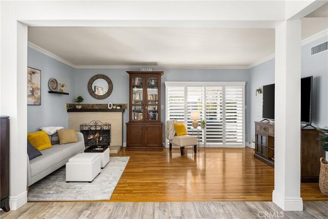 living area featuring visible vents, baseboards, a lit fireplace, ornamental molding, and wood finished floors