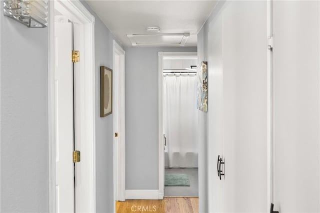 corridor with attic access, light wood-style floors, and baseboards