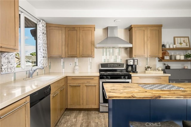 kitchen with butcher block counters, light wood-type flooring, stainless steel appliances, wall chimney exhaust hood, and a sink