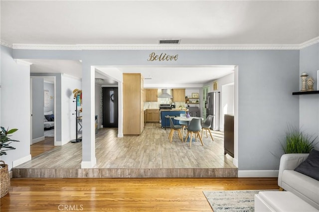 living area with visible vents, light wood-type flooring, baseboards, and ornamental molding