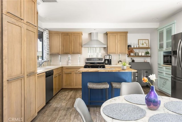 kitchen with a center island, wall chimney range hood, butcher block countertops, appliances with stainless steel finishes, and wood finished floors