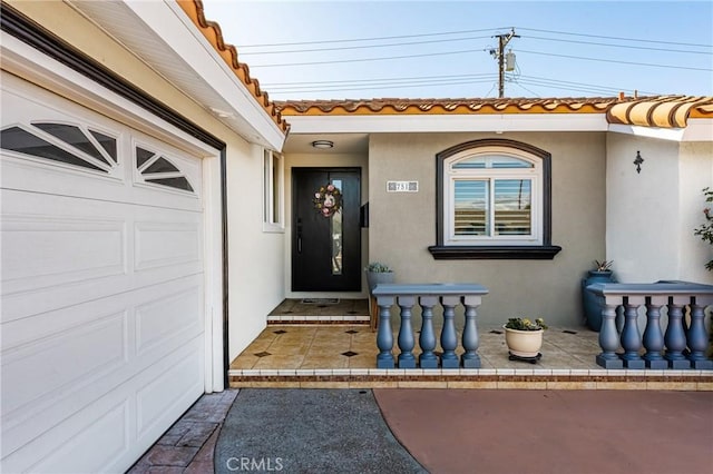 property entrance featuring a tile roof, a garage, and stucco siding