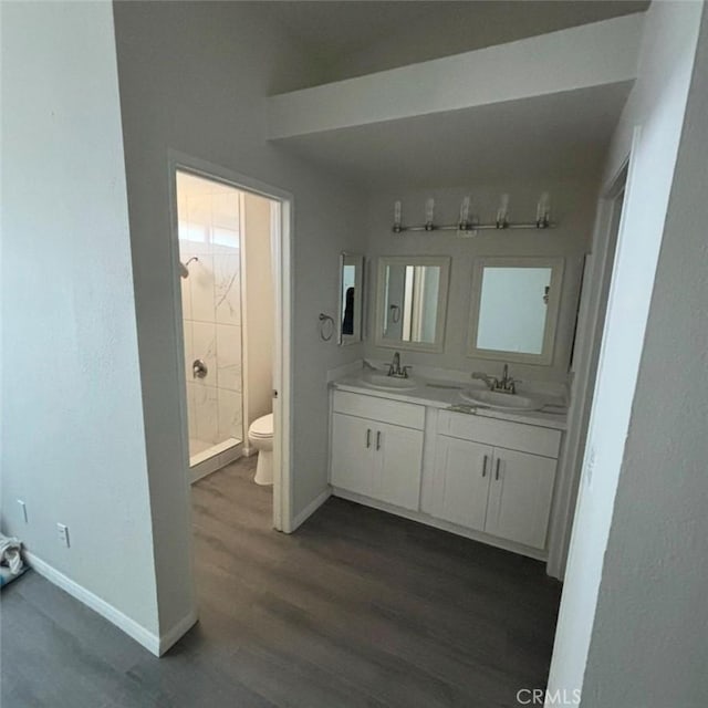 full bath with baseboards, toilet, double vanity, wood finished floors, and a sink