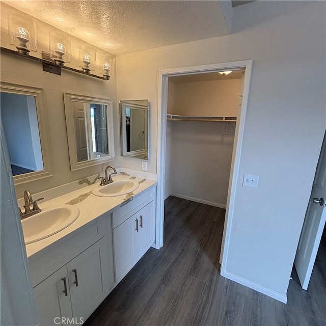 bathroom featuring a sink, a textured ceiling, wood finished floors, and double vanity