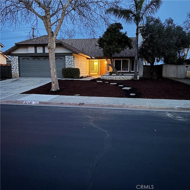 view of front of home featuring stone siding, concrete driveway, an attached garage, and fence