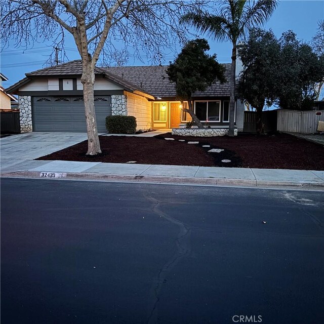 view of front of house with a garage, stone siding, concrete driveway, and fence