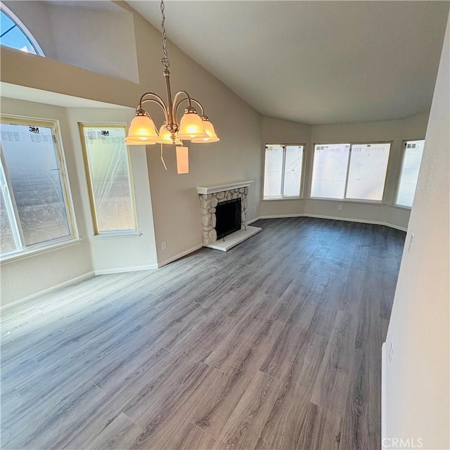 unfurnished living room with wood finished floors, baseboards, lofted ceiling, a fireplace, and a chandelier