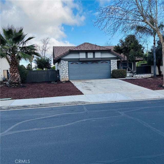 view of front of house featuring fence, a tiled roof, concrete driveway, a garage, and stone siding