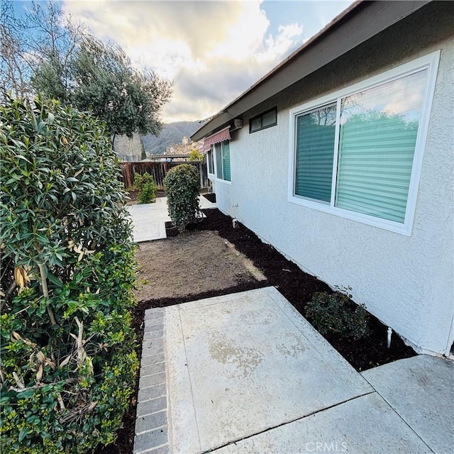 view of side of home featuring stucco siding, a patio, and fence