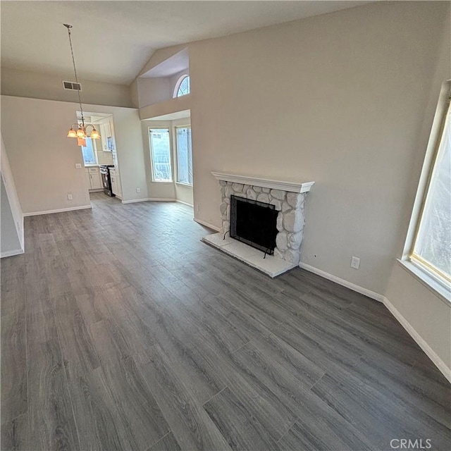 unfurnished living room featuring baseboards, visible vents, dark wood finished floors, a stone fireplace, and a chandelier