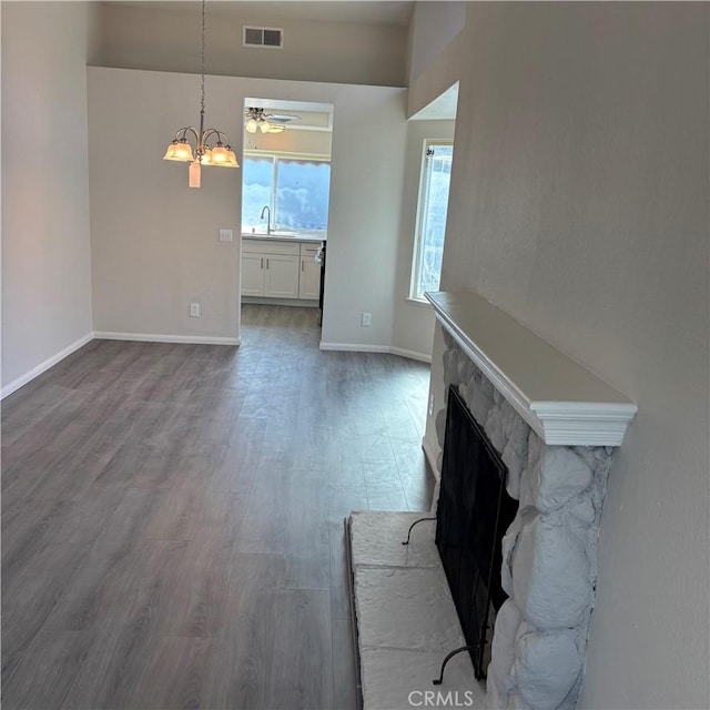 unfurnished living room featuring wood finished floors, baseboards, visible vents, a fireplace, and a sink