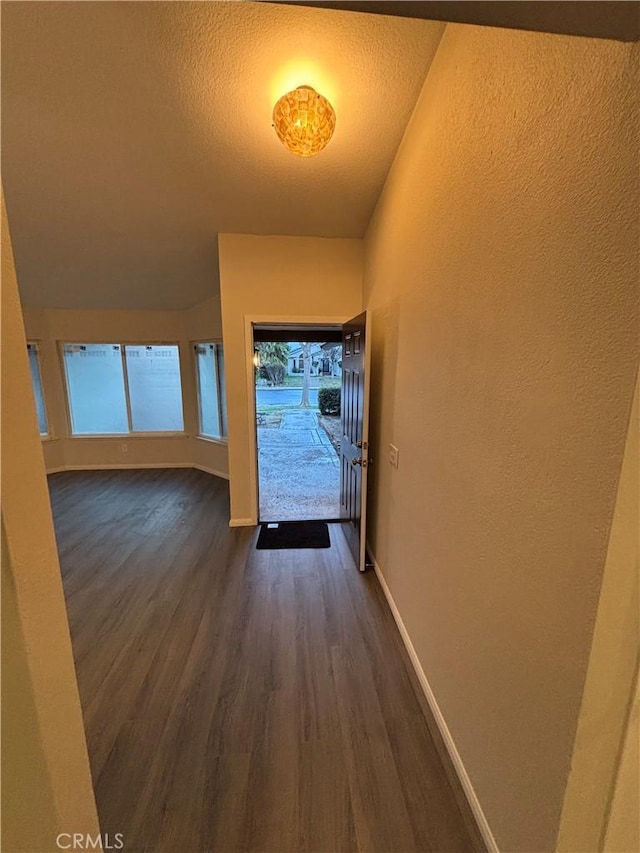 interior space with baseboards, a textured ceiling, dark wood finished floors, and a textured wall