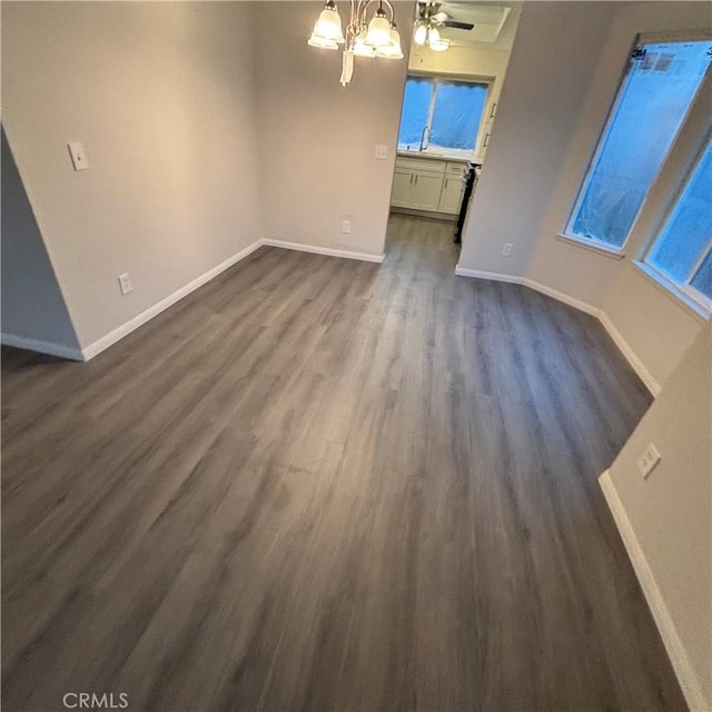 unfurnished living room featuring baseboards, a chandelier, and dark wood-style flooring