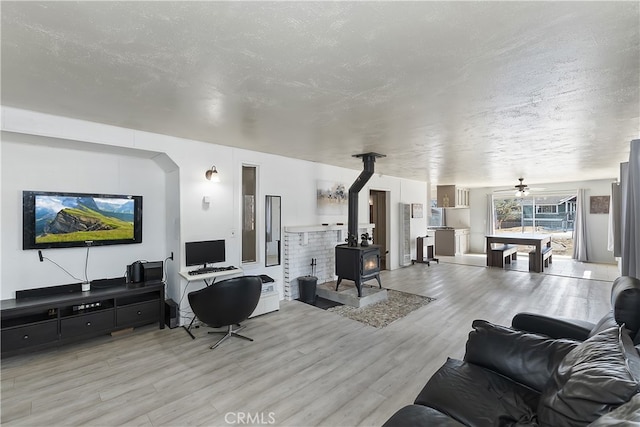 living room featuring a textured ceiling, light wood-type flooring, a wood stove, and ceiling fan