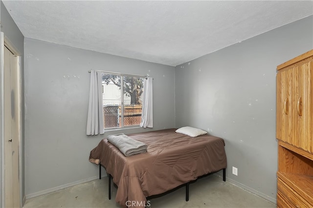 bedroom with a textured ceiling, concrete flooring, and baseboards