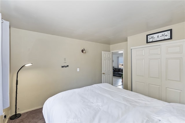 bedroom featuring baseboards, dark colored carpet, and a closet