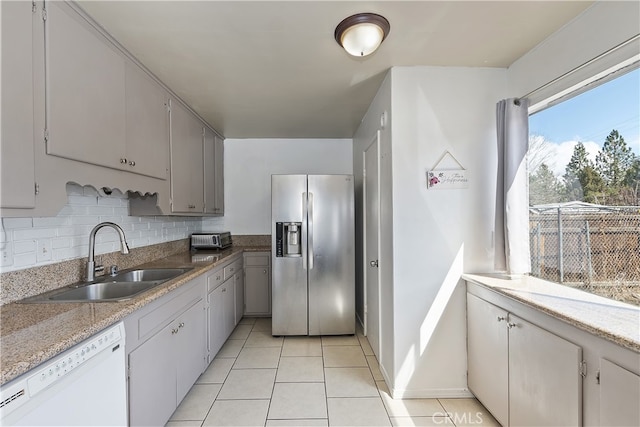 kitchen featuring backsplash, dishwasher, stainless steel refrigerator with ice dispenser, light tile patterned flooring, and a sink