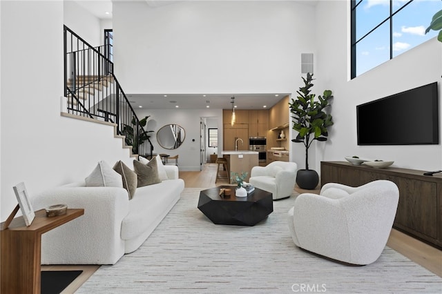 living area featuring light wood-type flooring, a towering ceiling, and stairs