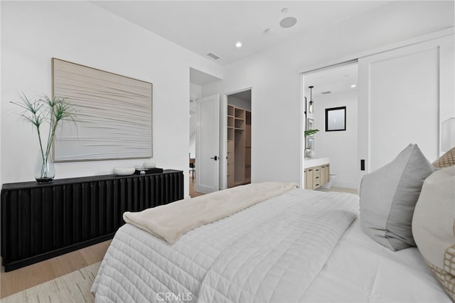 bedroom with connected bathroom, a walk in closet, radiator heating unit, recessed lighting, and light wood-style floors