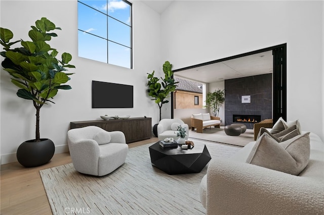 living area featuring a tiled fireplace, a healthy amount of sunlight, a high ceiling, and wood finished floors