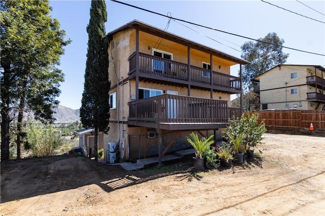 rear view of property featuring a balcony, fence, and stucco siding