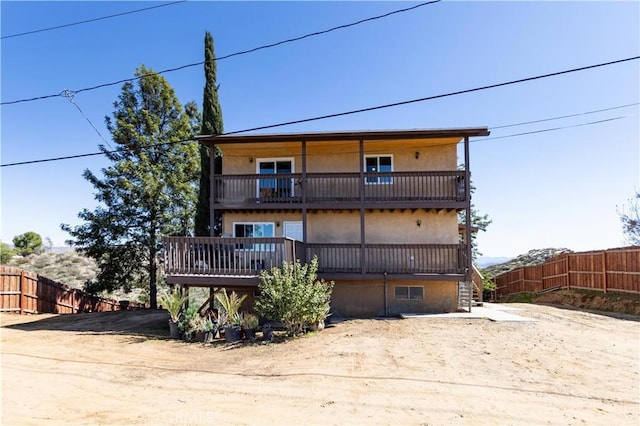 rear view of house featuring stucco siding, a balcony, and fence