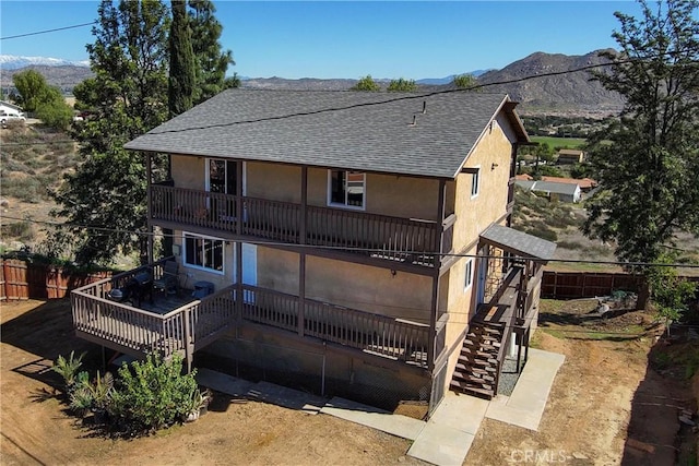 back of house with stucco siding, roof with shingles, stairs, and fence