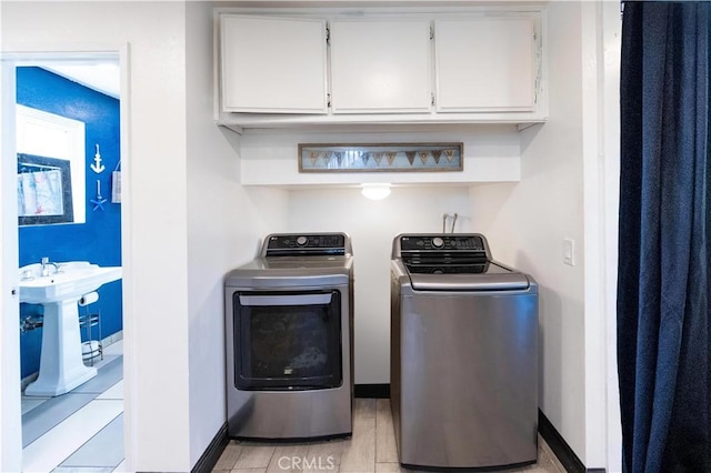 clothes washing area with a sink, baseboards, cabinet space, and washing machine and clothes dryer