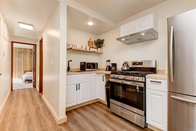 kitchen with light wood finished floors, a sink, light countertops, under cabinet range hood, and appliances with stainless steel finishes