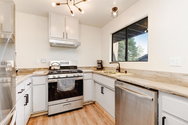 kitchen with a sink, white cabinets, light wood-style floors, under cabinet range hood, and appliances with stainless steel finishes