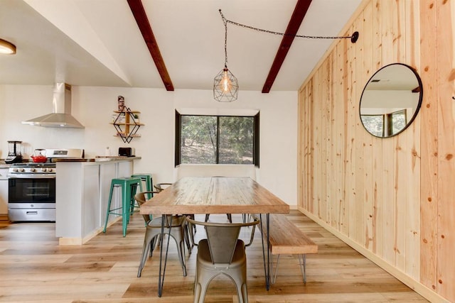 dining area with lofted ceiling with beams, baseboards, wooden walls, and light wood finished floors