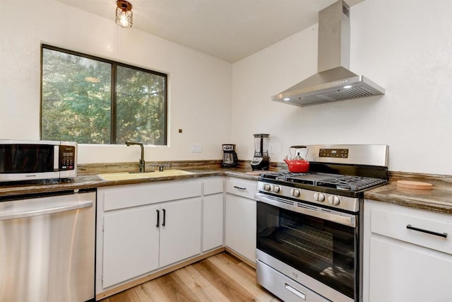 kitchen featuring light wood-type flooring, a sink, white cabinetry, stainless steel appliances, and wall chimney exhaust hood