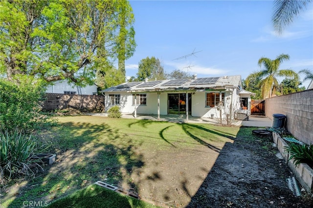 back of house featuring solar panels, a yard, a fenced backyard, stucco siding, and a patio area