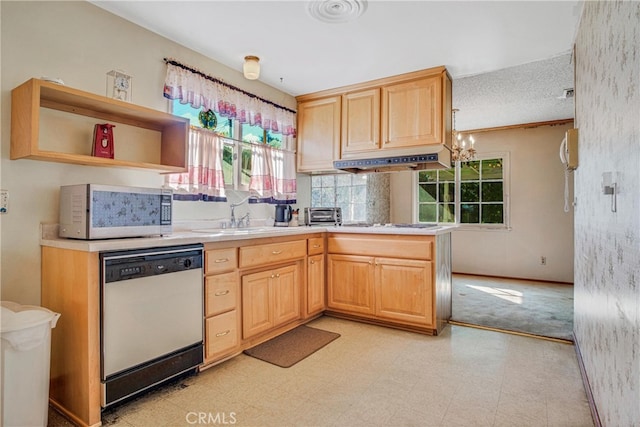 kitchen with light brown cabinets, under cabinet range hood, light floors, dishwasher, and a sink