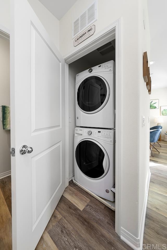 laundry area featuring visible vents, stacked washer and clothes dryer, laundry area, and wood finished floors